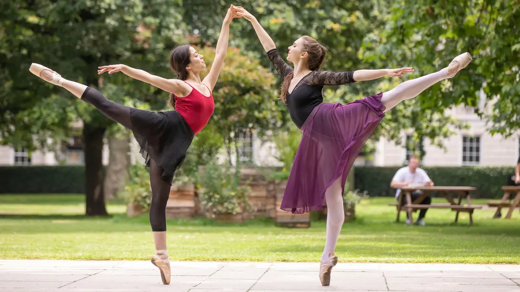 Two ballerinas performing poses outdoors in a green park setting