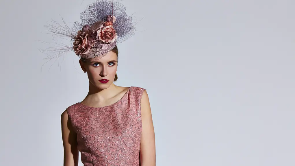 A woman wearing a pink sleeveless dress and a pink hat with roses and lace