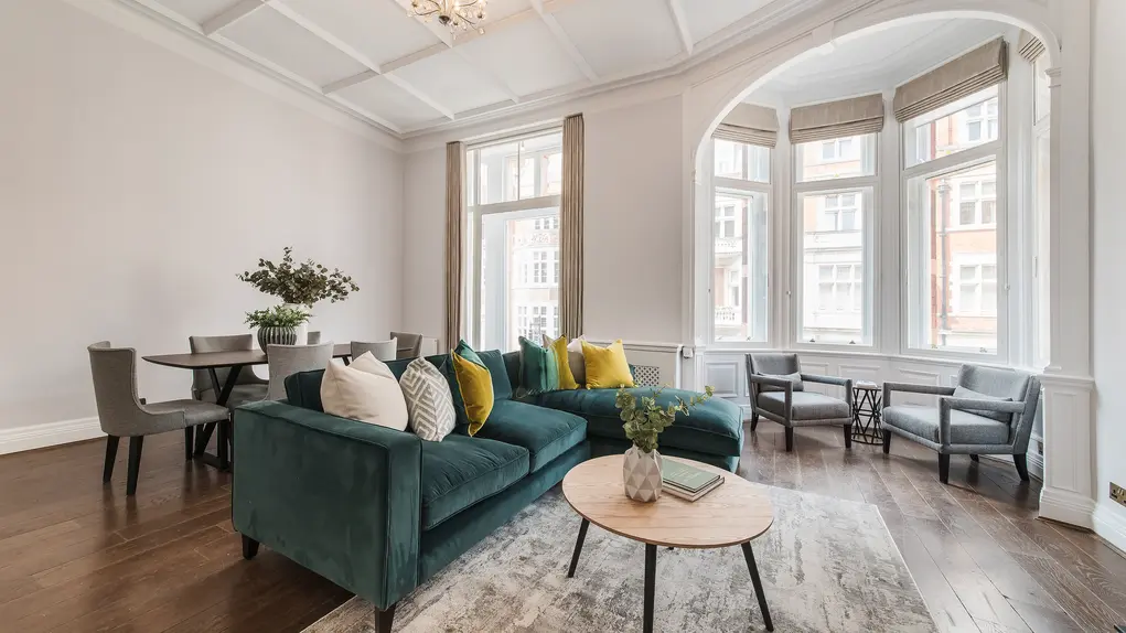 A living room with large windows, high ceilings and a teal corner sofa