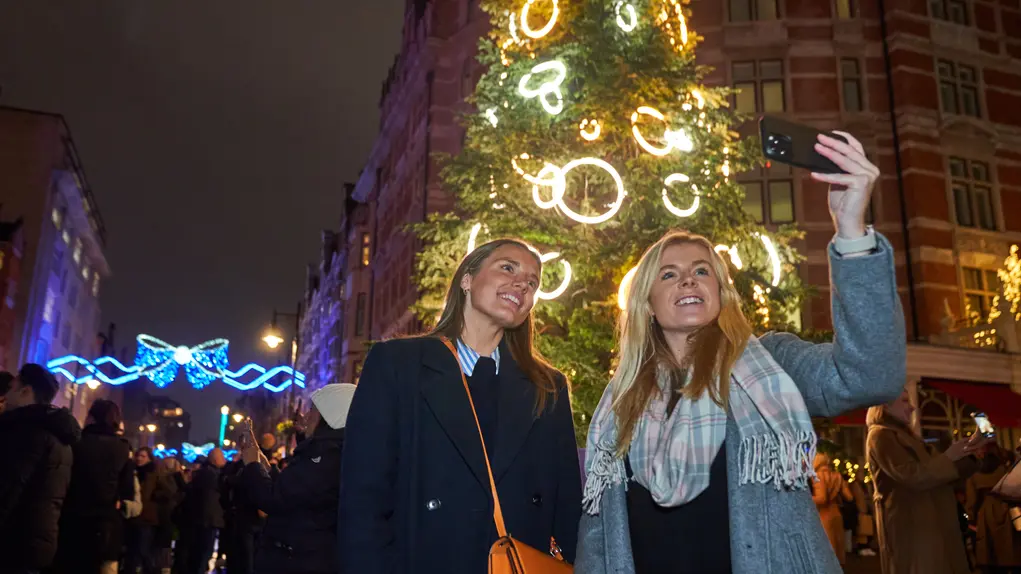 Two women take a selfie in front of a large Christmas tree