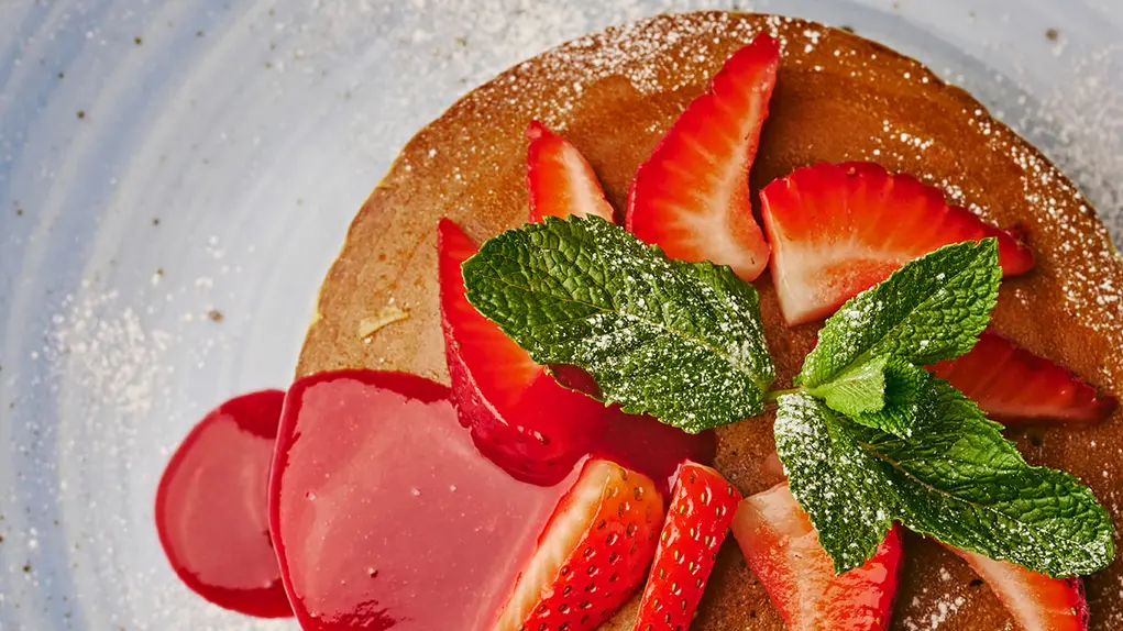 Pancakes topped with strawberries and mint and strawberry sauce