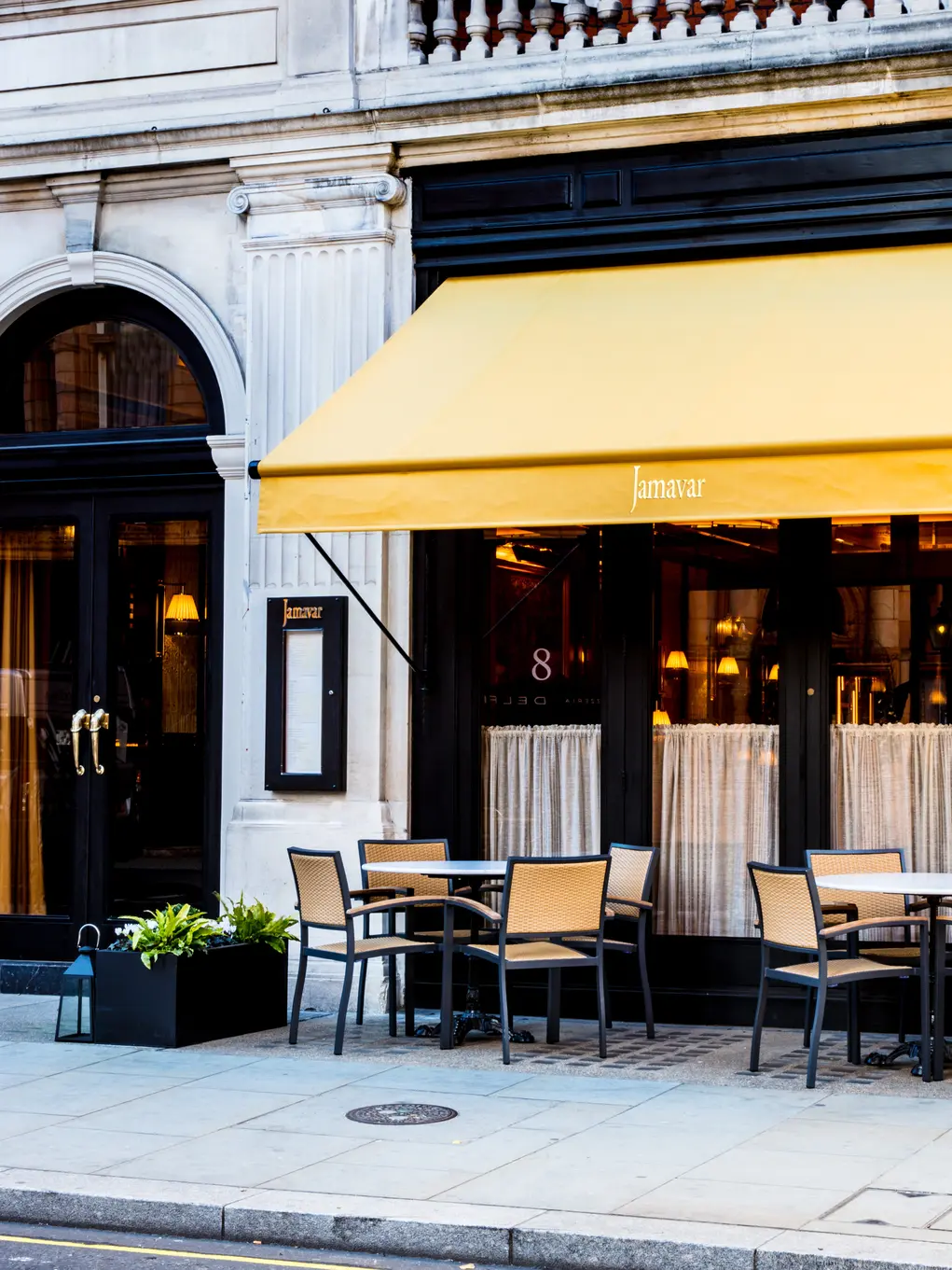 The exterior of Jamavar with yellow awning and chairs and tables outside