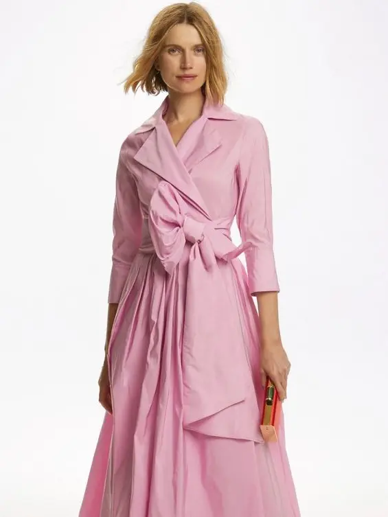 A woman is wearing a long pink dress with a big bow tied at the middle