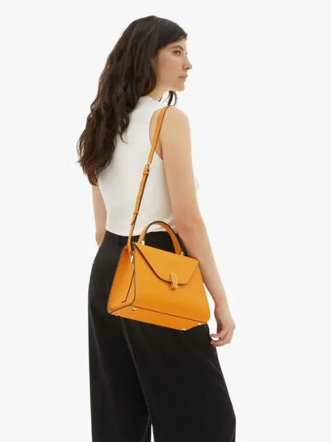 A woman wearing a white sleeveless top, black trousers and a yellow handbag
