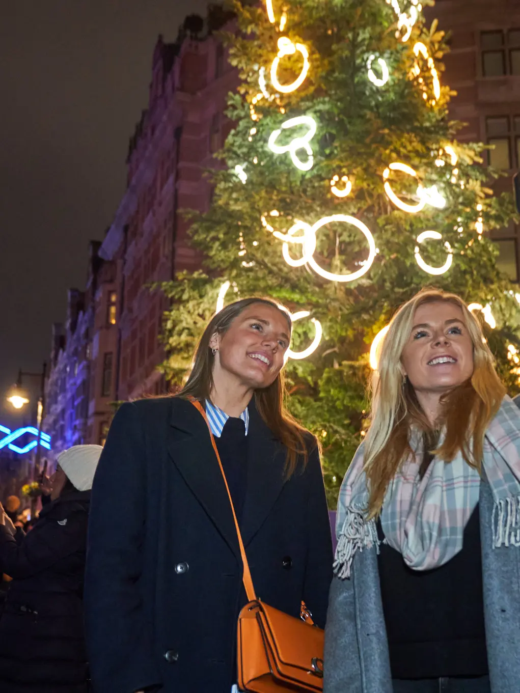 Two women take a selfie in front of a large Christmas tree