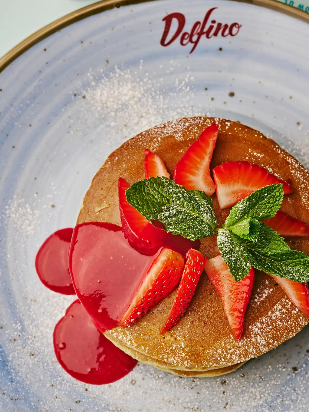 Pancakes topped with strawberries and mint and strawberry sauce
