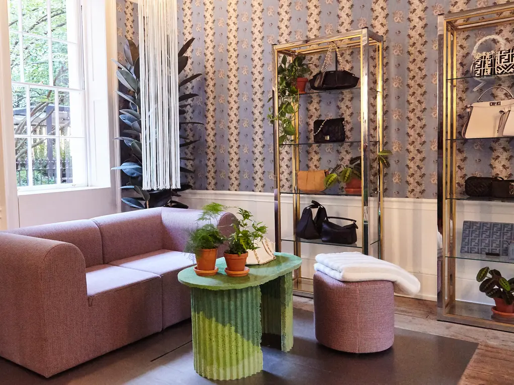 The inside of Browns with a pink sofa and gold shelves containing handbags