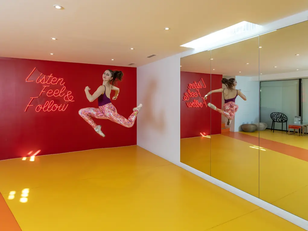 Dance studio with a yellow floor, red wall with artwork showing woman jumping in the air, and a mirror on the right wall