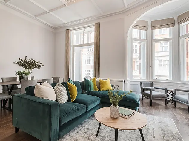 Living room with large windows, high ceilings, a teal sofa and dining table
