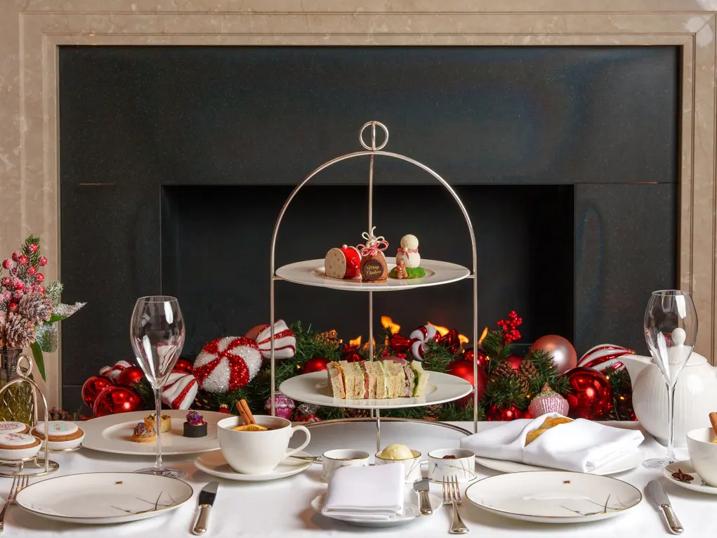 A tiered cake tray with cakes and a table set for afternoon tea in front of a fireplace