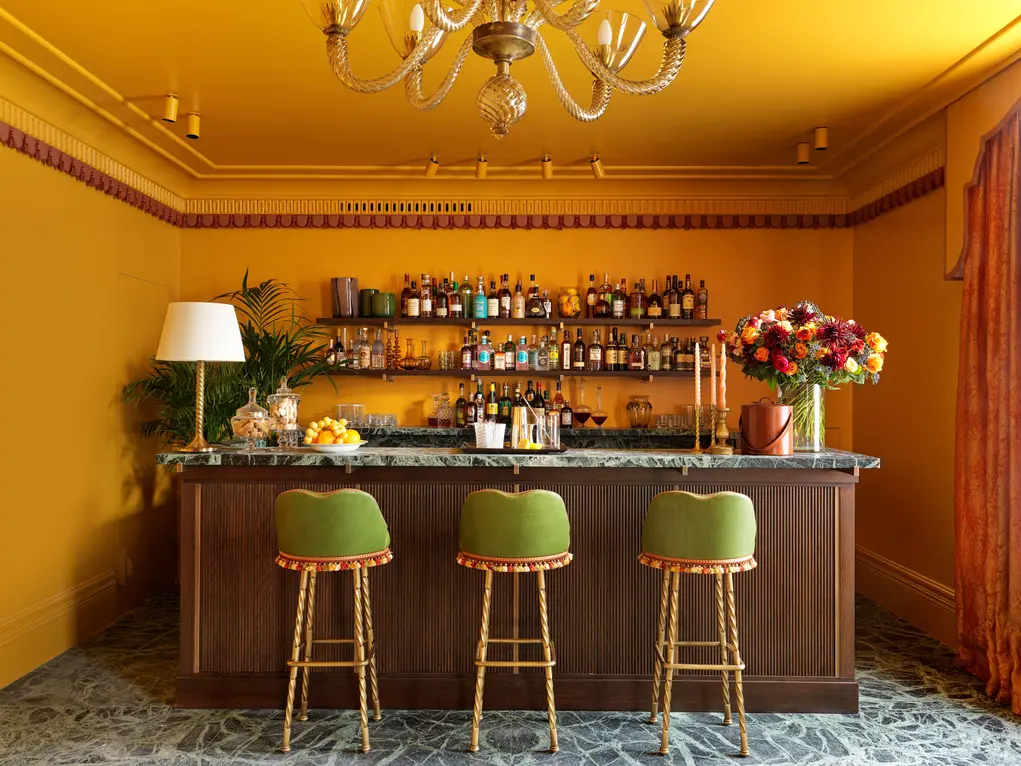 A bar with yellow walls and three green bar stools 