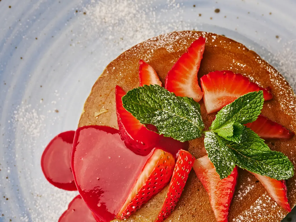 Pancakes topped with strawberries and mint and strawberry sauce
