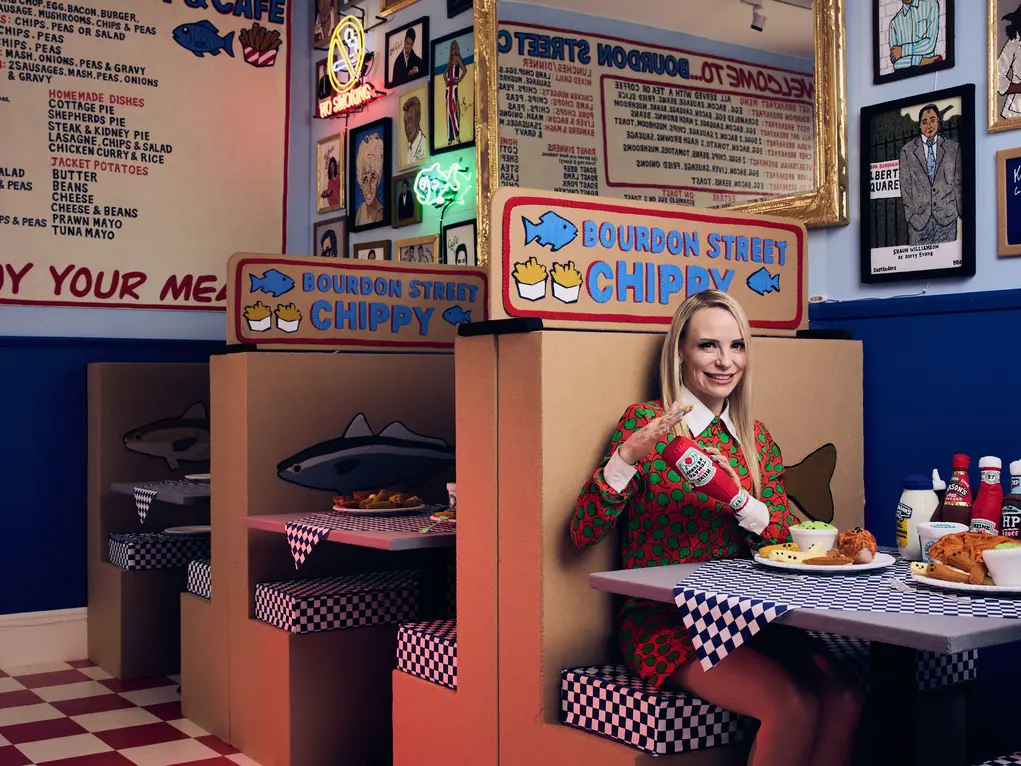 Lucy Sparrow sitting in a booth in her fish and chip shop installation 