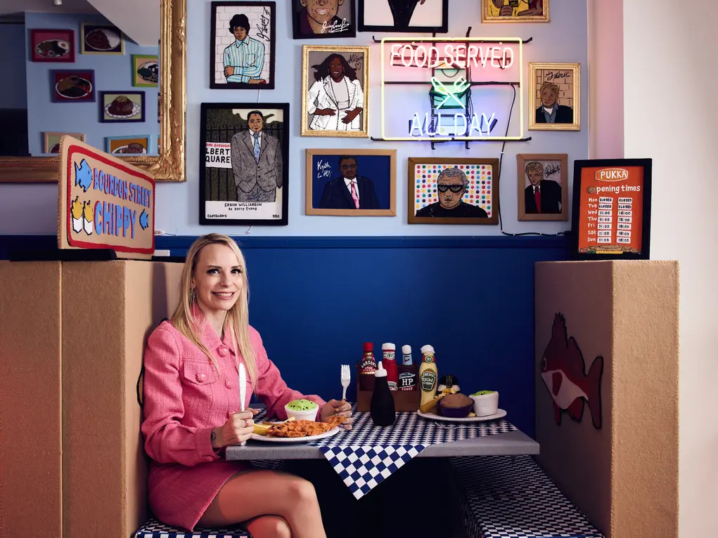 Artist Lucy Sparrow sitting in a booth in her fish and chip shop installation 