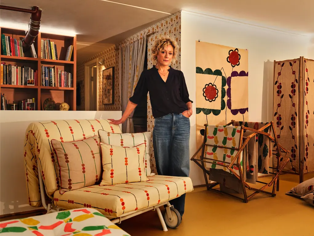 A woman stands in a living room with bookshelves and artwork